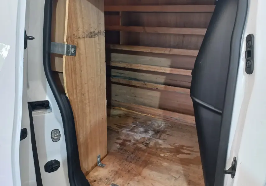 Vue intérieure du coffre arrière ouvert d’un utilitaire Peugeot Partner blanc, montrant la cloison et le plancher en bois.