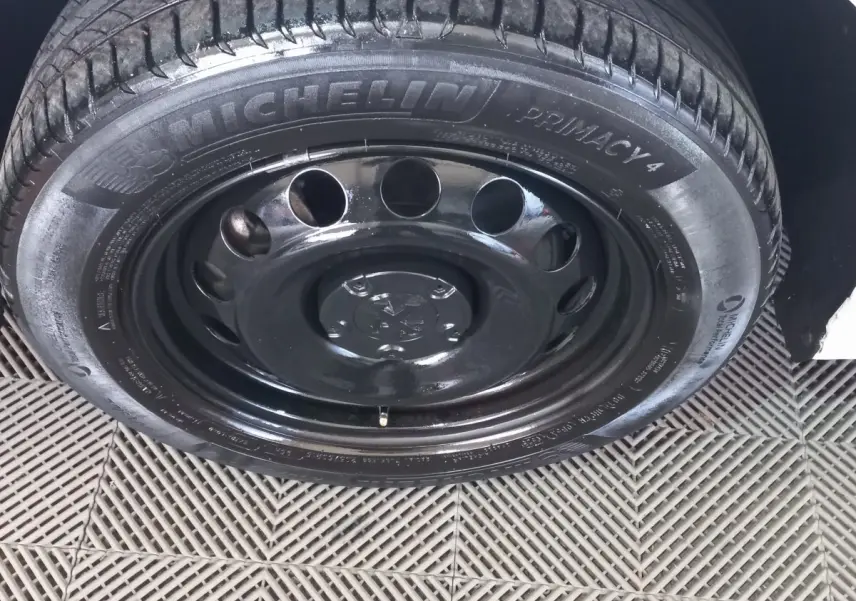 Gros plan sur la roue avant droite avec jante acier noire et pneu Michelin du Peugeot Partner blanc.