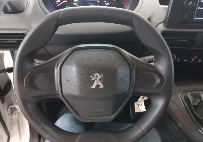 Vue rapprochée du volant noir avec logo Peugeot au centre, tableau de bord et levier de vitesses d’un Partner blanc 2021.