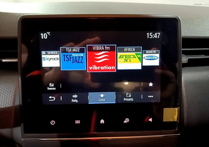 Écran tactile central de la Renault Clio gris clair, affichant les stations radio avec interface moderne.