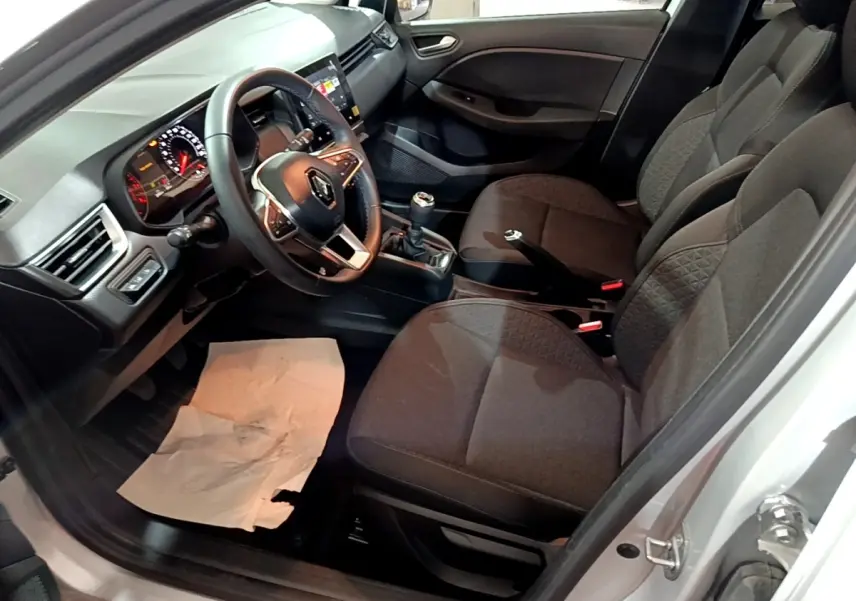 Vue intérieure côté conducteur de la Renault Clio gris clair 2023, volant cuir, tableau de bord avec écran tactile et boîte manuelle.