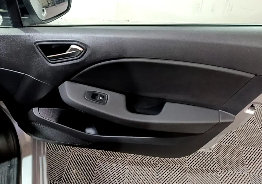 Vue intérieure du panneau de porte côté gauche gris foncé de la Renault Clio 2023, avec poignée et commande de vitre électrique.