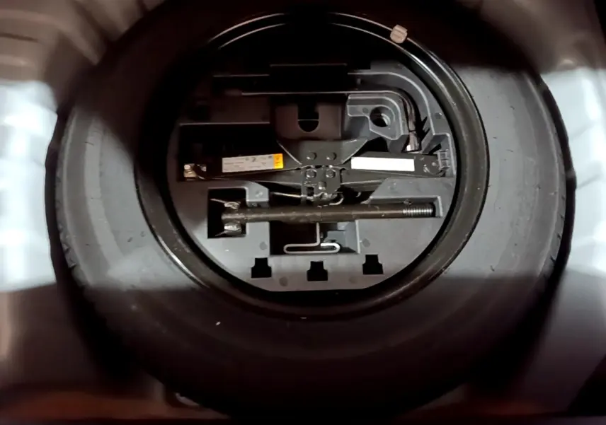 Gros plan sur la roue de secours noire et son outillage dans le coffre d'une Renault Clio gris clair 2023.