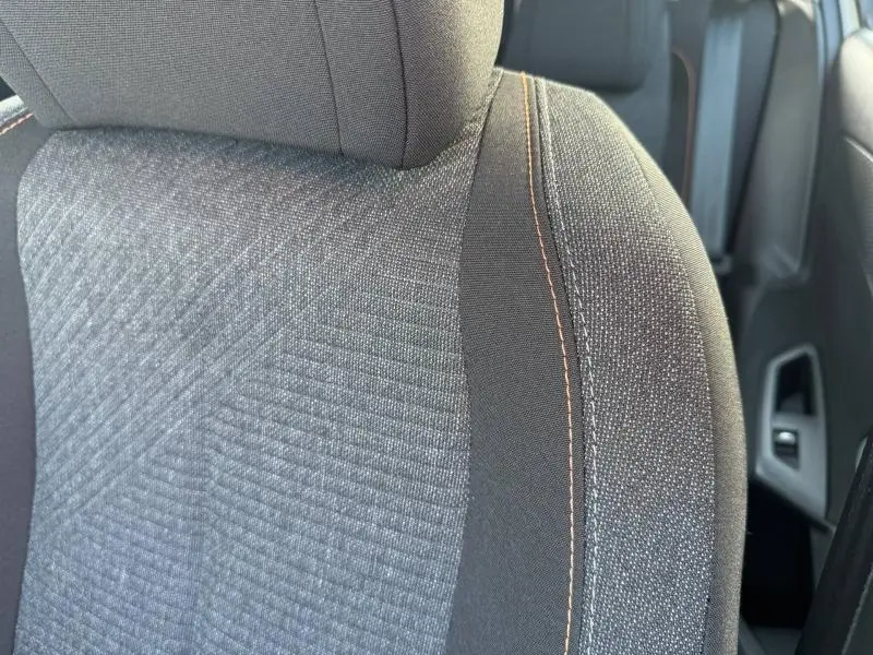 Gros plan sur le siège avant en tissu gris avec surpiqûres orange de la Peugeot 308 2025 côté droit.