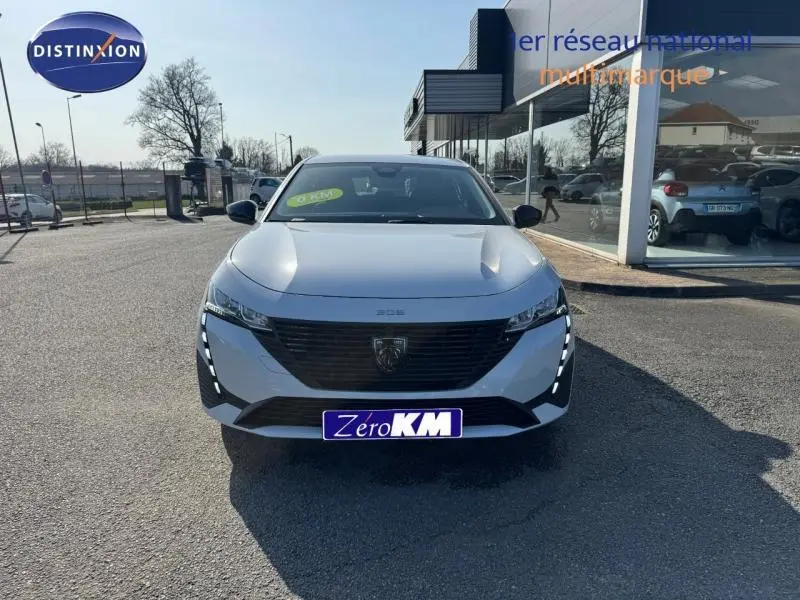 Vue avant frontale d'une Peugeot 308 blanche Okénite avec calandre noire et feux LED verticaux allumés.