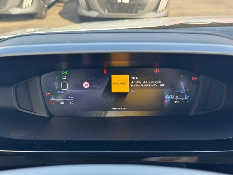 Affichage numérique du tableau de bord de la Peugeot 308 blanc Okénite, avec informations de conduite et radio visibles.