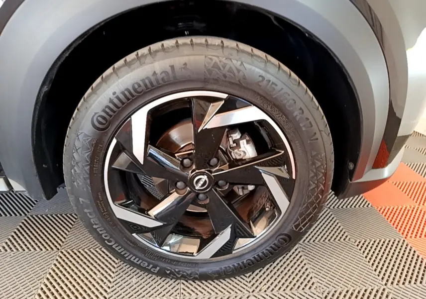 Gros plan sur la roue avant droite noire du Nissan Juke 2022 avec jante alliage au design géométrique.