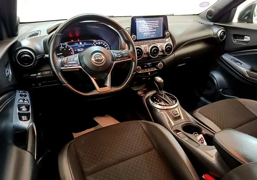 Vue intérieure côté conducteur du tableau de bord et console centrale du Nissan Juke noir avec écran tactile et volant multifonctions.