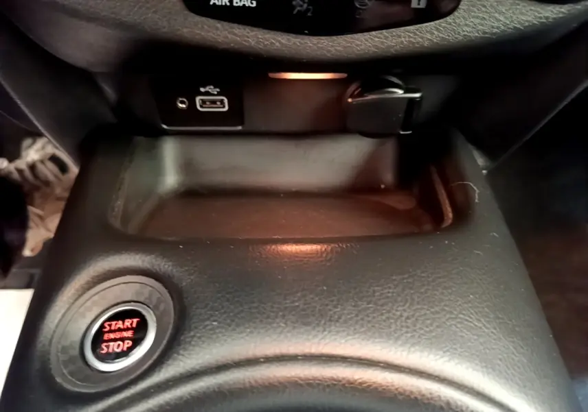 Gros plan intérieur sur la console centrale noire du Nissan Juke 2022 avec bouton start/stop rouge et prise USB visible.