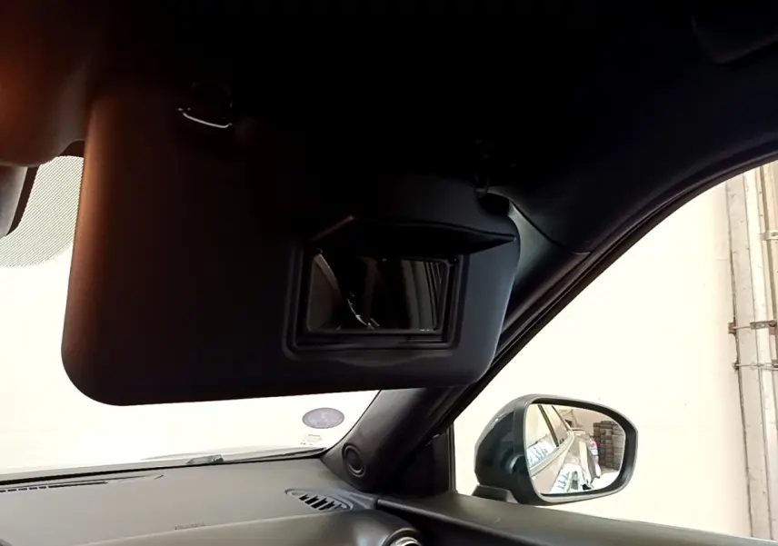 Intérieur du Nissan Juke 2022 noir, vue côté passager avec pare-soleil baissé et rétroviseur extérieur visible.