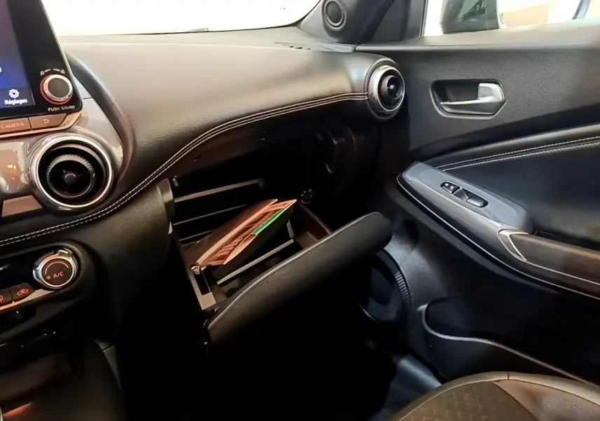 Vue intérieure côté passager du tableau de bord noir du Nissan Juke 2022 avec boîte à gants ouverte et porte en similicuir.