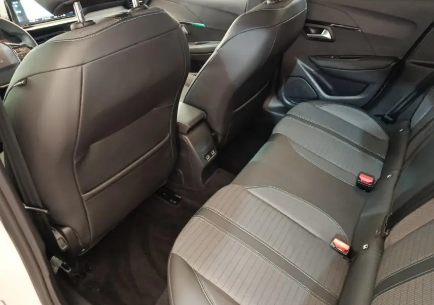 Vue intérieure arrière côté droit de la Peugeot 208 blanche, montrant la banquette et les sièges avant en cuir noir.