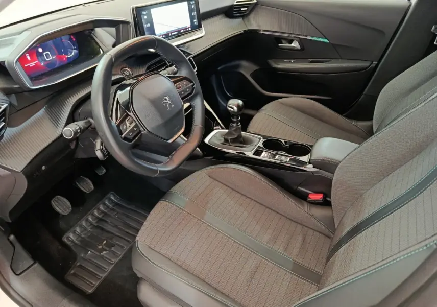 Vue intérieure côté conducteur de la Peugeot 208 2021, volant cuir, écran tactile 10 pouces et sièges gris.