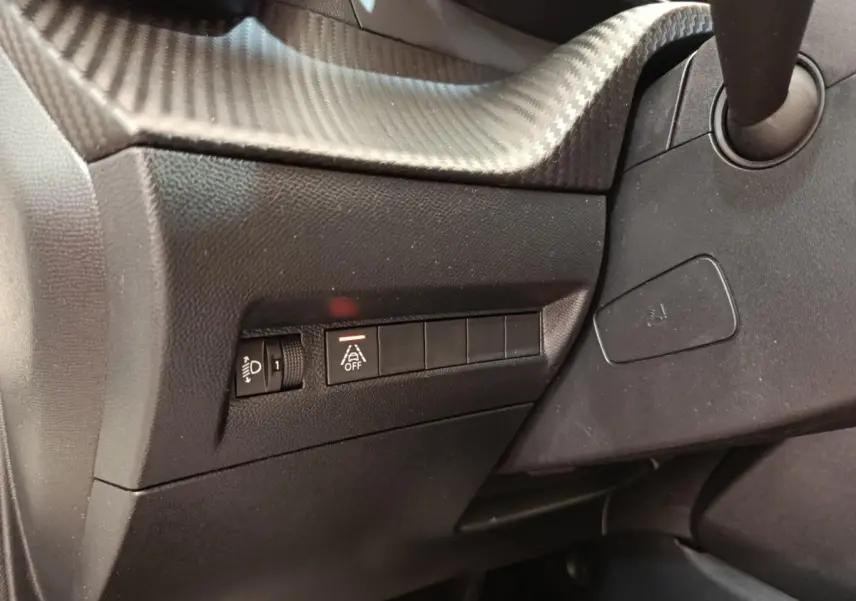 Détail du tableau de bord côté gauche de la Peugeot 208 blanche, avec commandes d'éclairage et d'aide à la conduite.