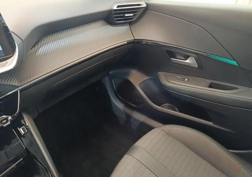 Vue intérieure côté passager de la Peugeot 208 PureTech 100 Allure Business, tableau de bord noir avec insert effet carbone.