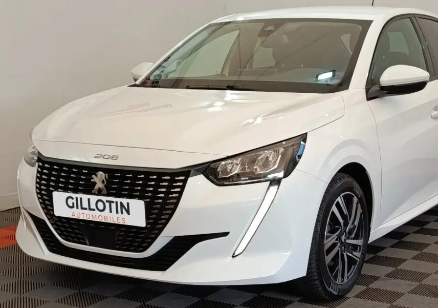 Peugeot 208 blanc vue 3/4 avant droit, avec calandre noire distinctive et feux LED en forme de griffes.