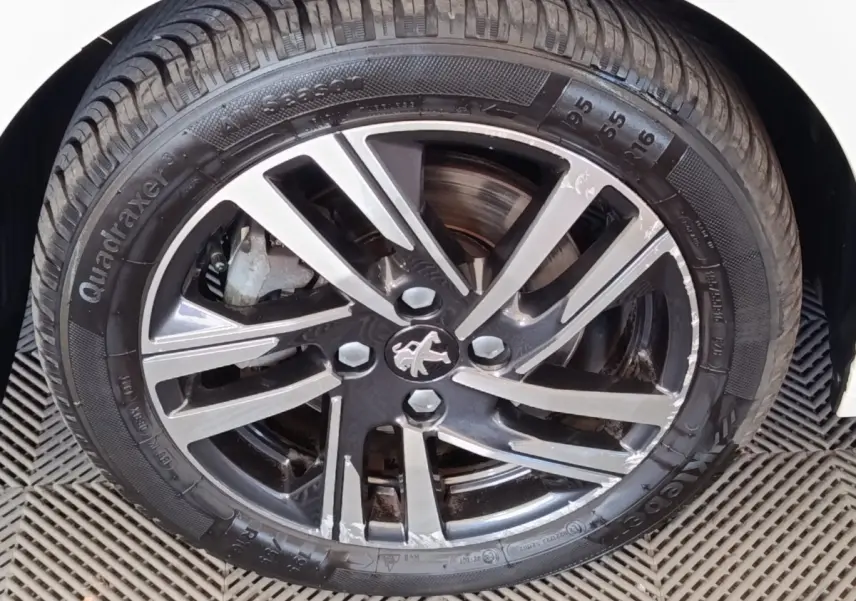 Gros plan sur la jante alliage bicolore et pneu noir du côté avant droit d’une Peugeot 208 blanche.