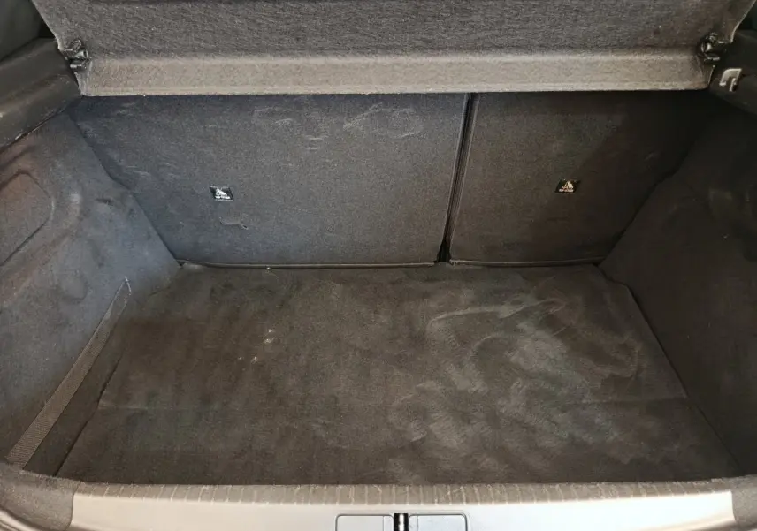 Coffre ouvert vu de face, intérieur noir, sans chargement, de la Peugeot 208 PureTech 100 S&S Allure Business blanche.