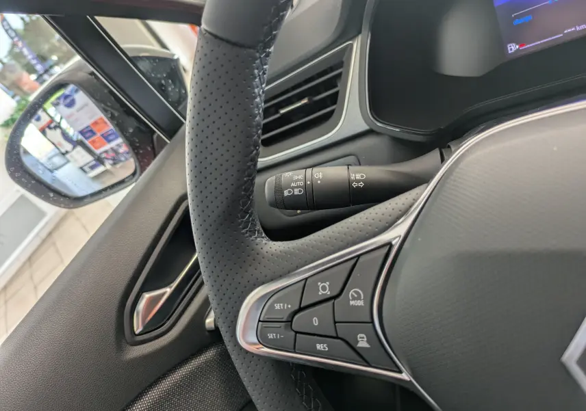 Gros plan sur le volant perforé et les commandes multifonctions du Renault Captur E-Tech rouge flamme, côté gauche intérieur.