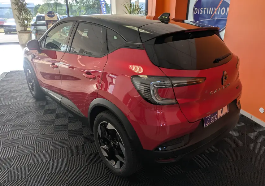 Vue 3/4 arrière droite d'un Renault Captur 2025 rouge flamme avec toit noir et jantes alliage 18 pouces noir brillant.