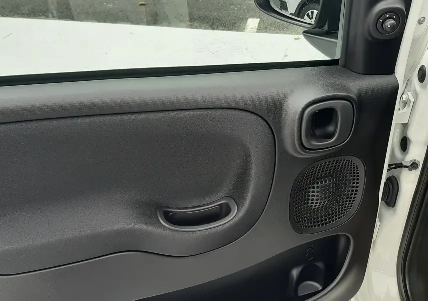 Vue intérieure de la porte avant droite d'une Fiat Panda 2025 blanc gelato, avec poignée et haut-parleur intégrés.