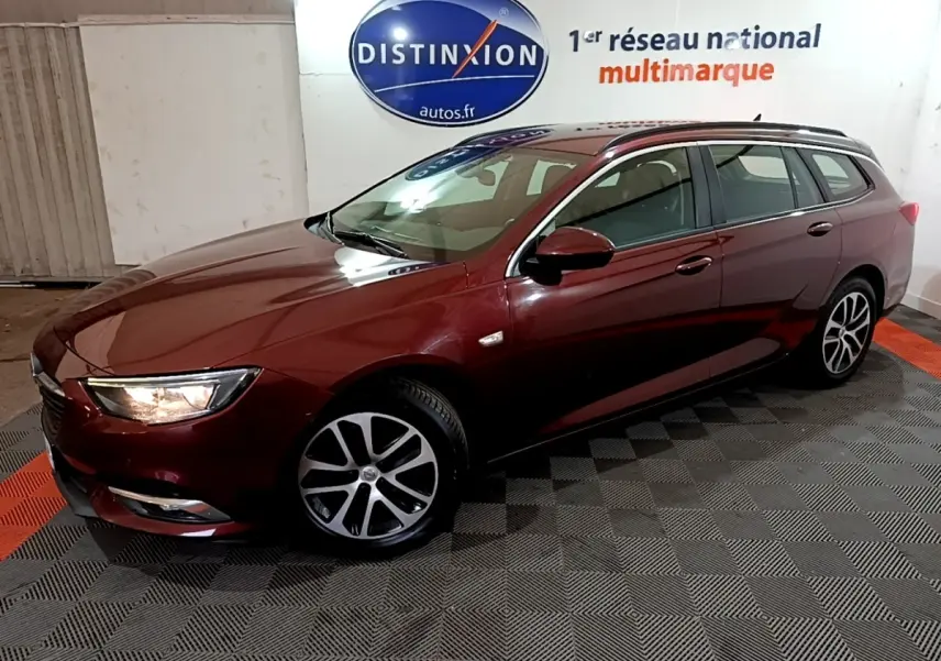Opel Insignia break rouge vue 3/4 avant droit avec jantes alliage et phares allumés en intérieur showroom.