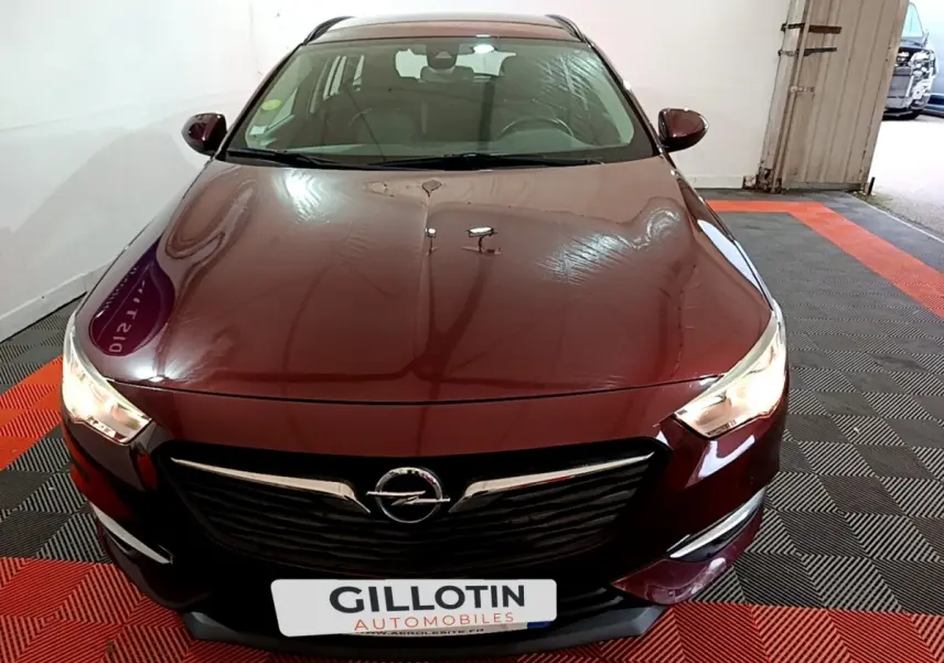 Vue avant d'une Opel Insignia rouge 2019 avec phares allumés et calandre chromée dans un garage.