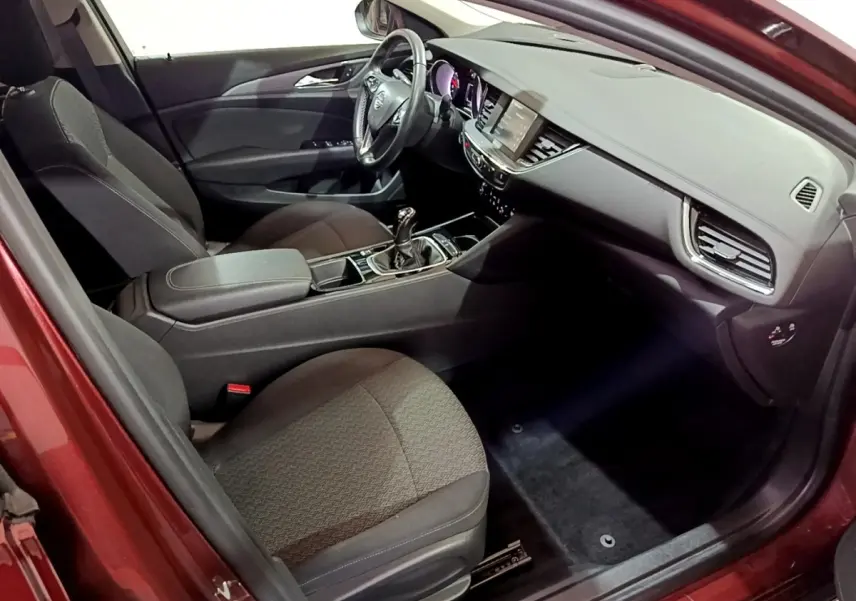 Vue intérieure côté conducteur de l’Opel Insignia rouge, montrant le tableau de bord et la console centrale avec boîte manuelle.