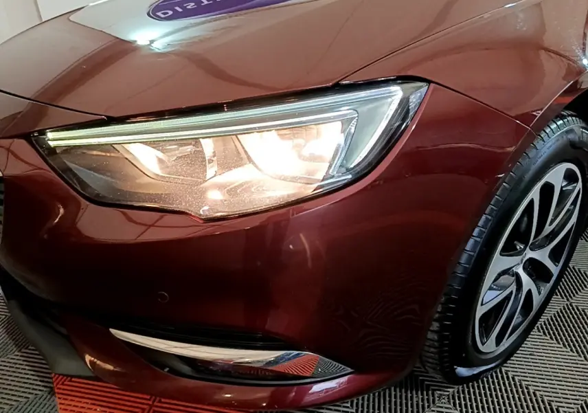 Gros plan sur le phare avant gauche et la roue d’une Opel Insignia rouge métallisée, finition Edition Business.