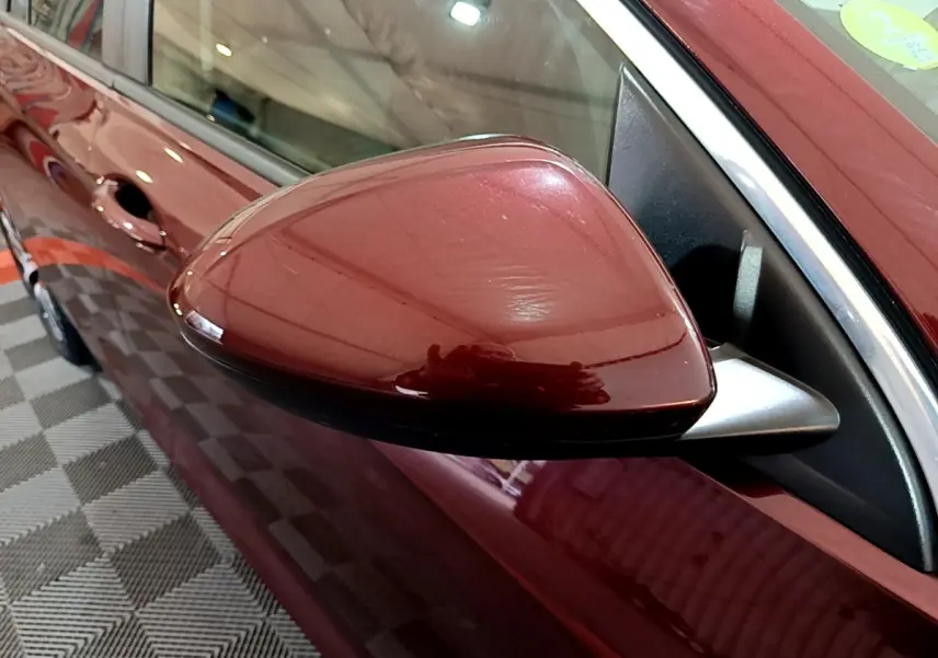 Gros plan sur le rétroviseur côté gauche de l’Opel Insignia rouge, montrant la portière et la poignée du véhicule.