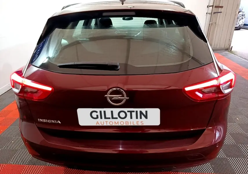 Vue arrière d'une Opel Insignia rouge avec feux allumés dans un garage au sol rouge et noir.