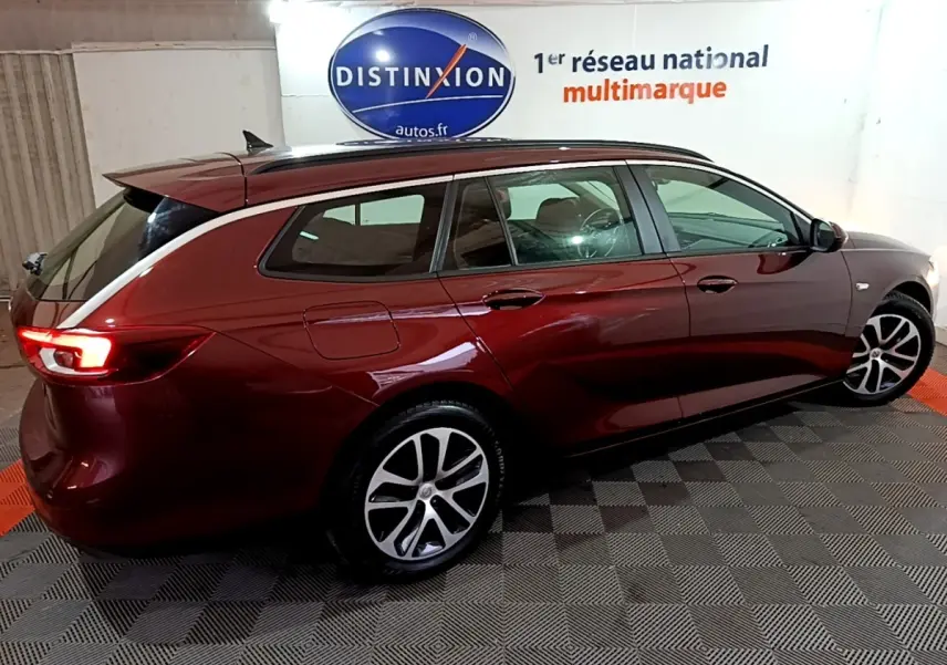 Opel Insignia rouge vue de profil côté droit, break avec jantes alliage et feux arrière allumés.
