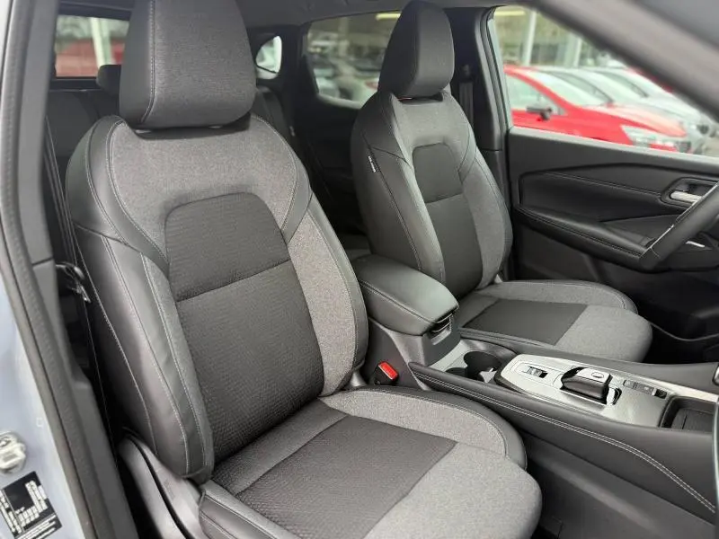 Vue intérieure du Nissan Qashqai Hybrid e-POWER 2025 montrant les sièges avant en tissu gris et console centrale avec boîte auto.
