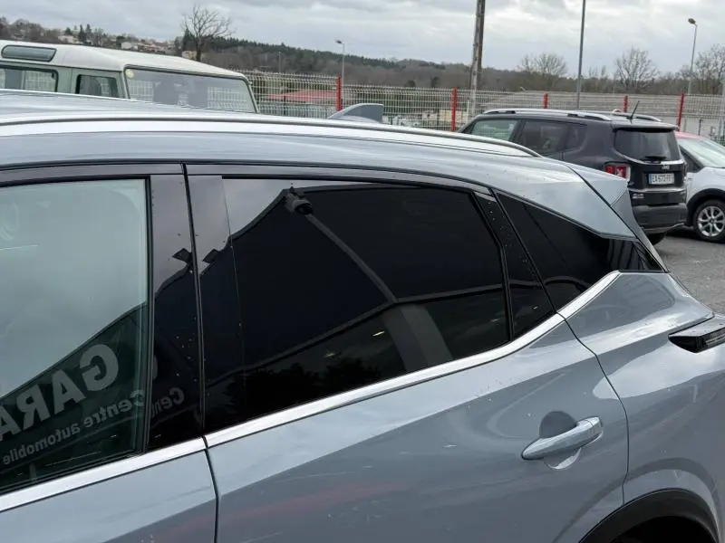 Vue latérale côté droit du Nissan Qashqai Hybrid e-POWER 2025 en gris argile avec vitres arrière teintées.