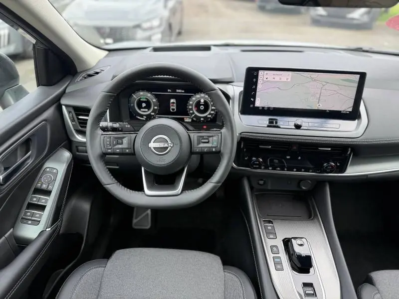 Vue intérieure avant du Nissan Qashqai Hybrid e-POWER 2025, tableau de bord moderne avec écran tactile et volant multifonction.