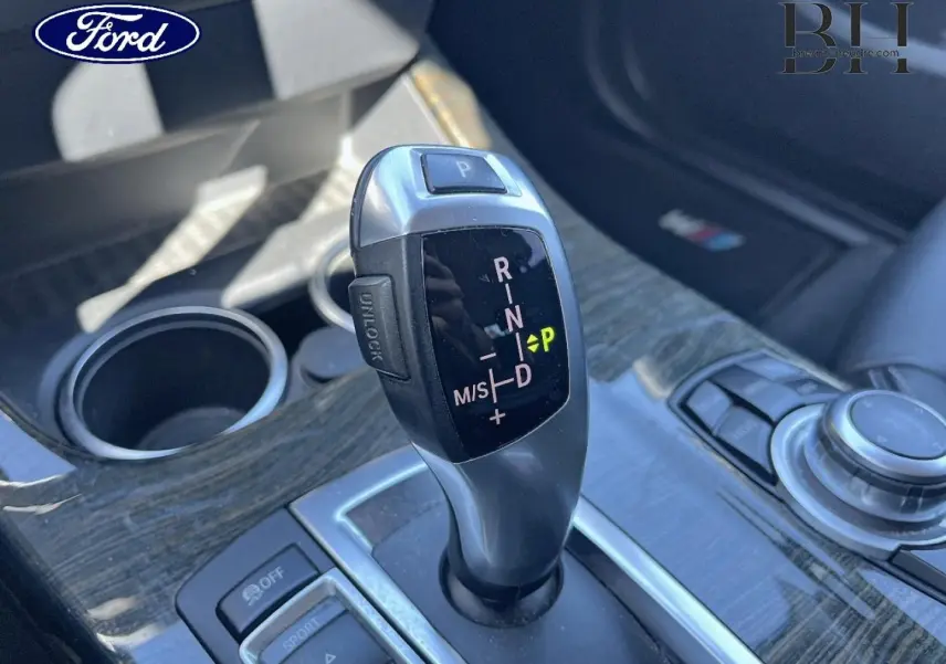 Levier de vitesse automatique BMW xDrive20dA en gros plan sur console bois, avec commandes et porte-gobelets visibles.
