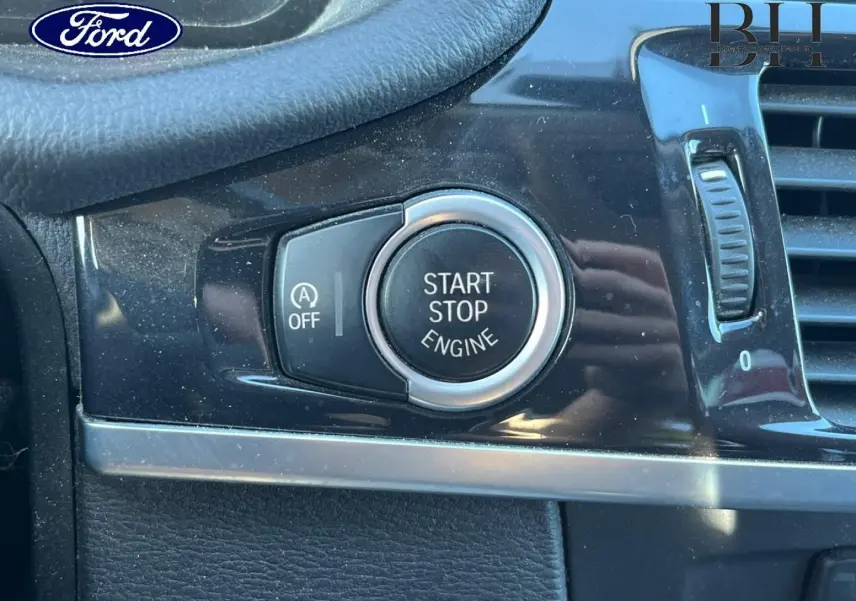 Bouton démarrage/arrêt moteur en gros plan sur tableau de bord noir brillant d'un BMW X3 Mineralsilber, vue intérieure rapprochée.
