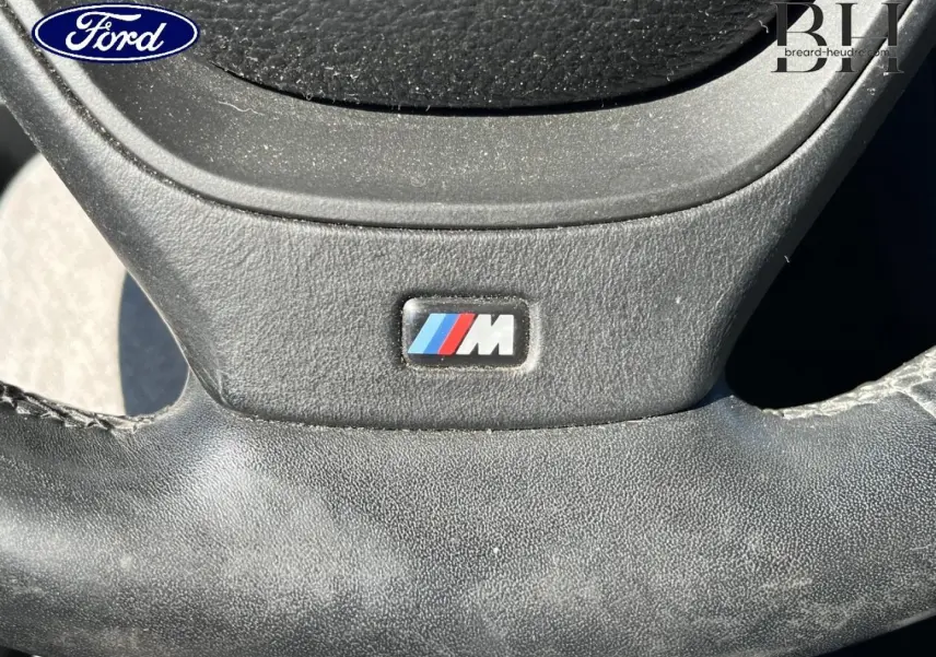 Gros plan sur le volant cuir avec logo M d'une BMW X3 Mineralsilber, mettant en valeur la finition sportive.
