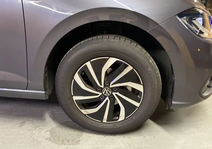 Gros plan sur la roue avant gauche d'une Volkswagen Polo gris métallisé avec jante alliage bicolore au design dynamique.