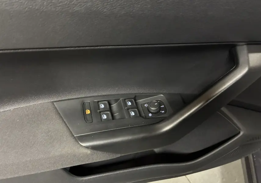 Gros plan sur la commande des vitres et réglages des rétroviseurs côté conducteur d'une Volkswagen Polo gris intérieur noir.