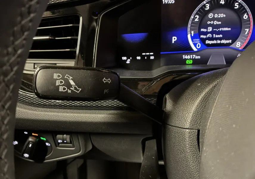 Gros plan sur la manette de clignotant et tableau de bord numérique bleu d'une Volkswagen Polo gris, intérieur noir.