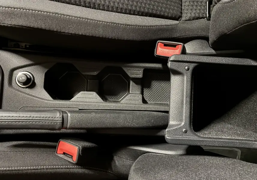 Gros plan sur la console centrale noire de la Volkswagen Polo gris, avec porte-gobelets et frein à main visible.