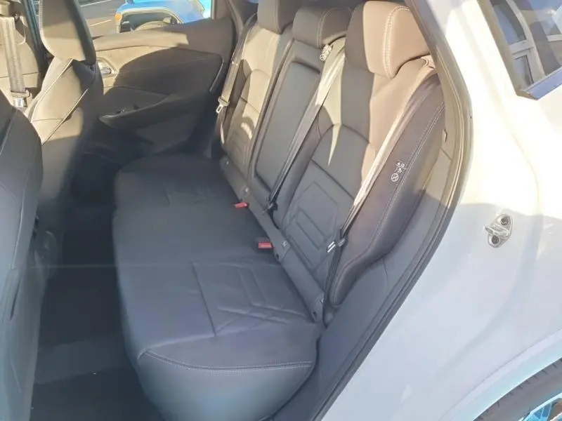Vue latérale de la banquette arrière en cuir noir du Nissan Qashqai blanc nacré, avec sièges individuels et ceintures visibles.