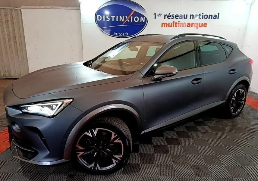 CUPRA Formentor gris foncé en 3/4 avant droit, avec jantes noires et phares LED allumés en intérieur showroom.