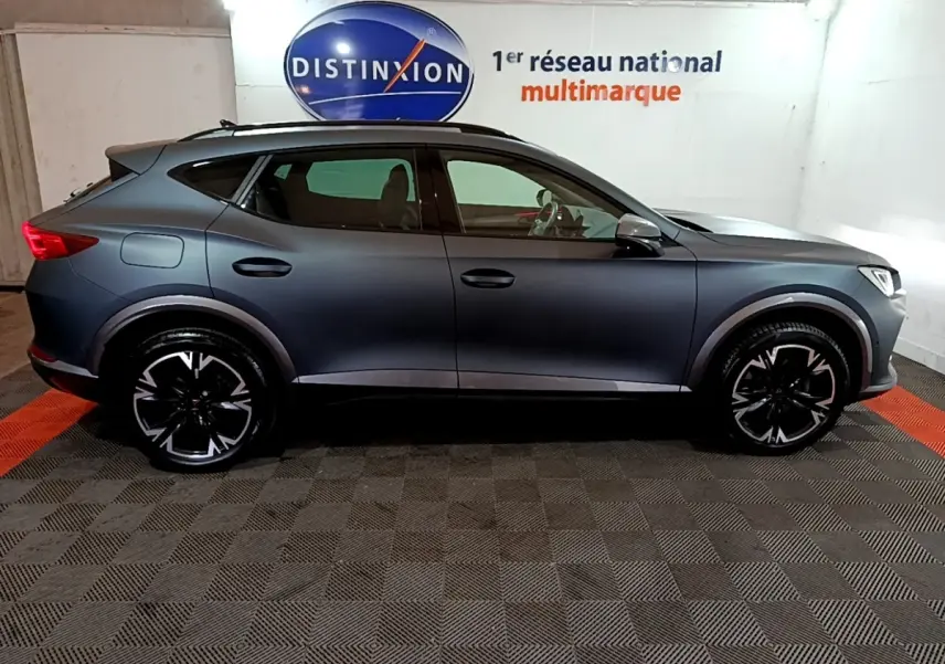 Vue de profil côté gauche d’un CUPRA Formentor gris foncé 2024 avec jantes noires et toit ouvrant en intérieur showroom.