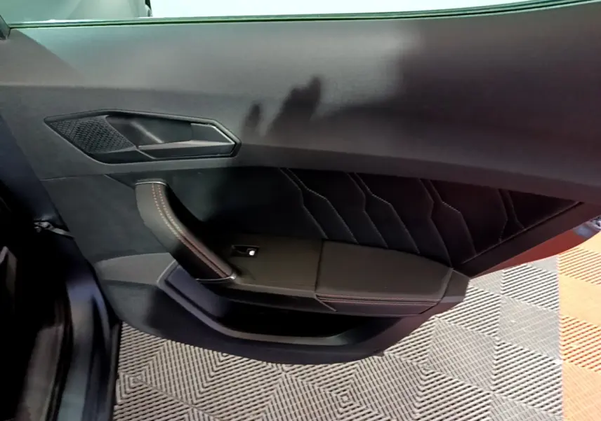 Vue intérieure de la porte avant gauche de la CUPRA Formentor gris foncé, avec surpiqûres rouges et poignée design.