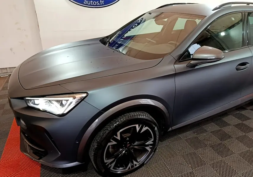 Vue 3/4 avant droit d'une CUPRA Formentor gris foncé avec jantes noires à motifs argentés et phares allumés.