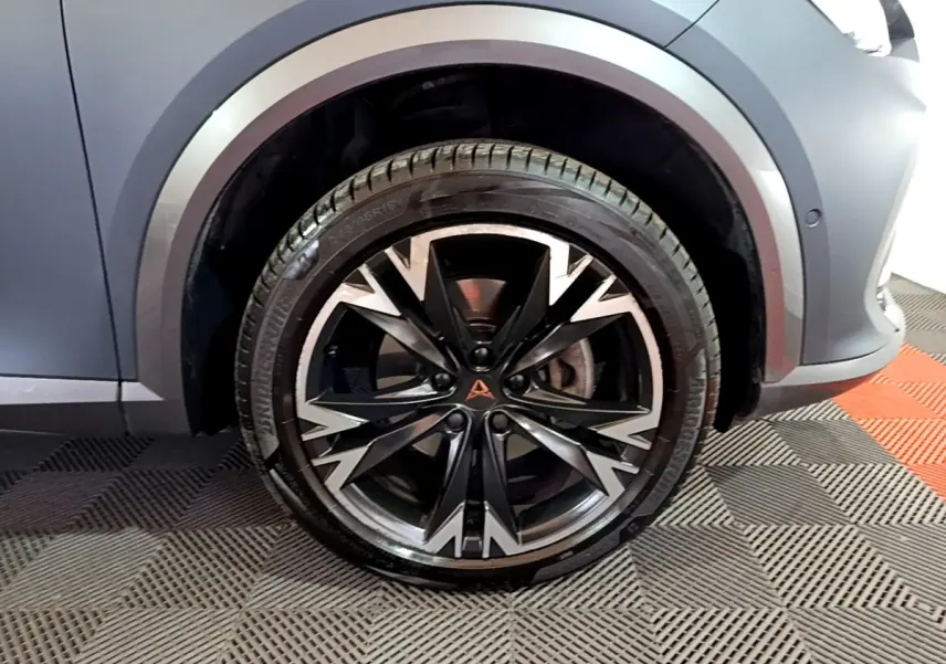 Gros plan sur la roue avant droite du CUPRA Formentor gris foncé, mettant en valeur la jante alu noire et argentée au design dynamique.
