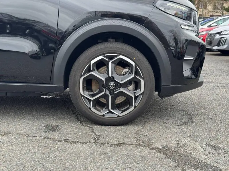 Gros plan sur la roue avant droite et partie avant d'une Citroën C3 électrique 2025 noir Perla Nera avec jante alu distinctive.