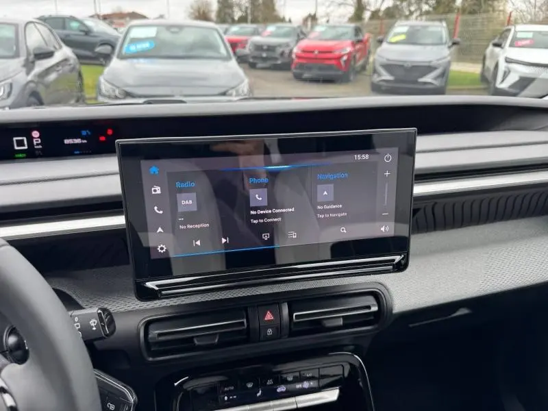 Vue intérieure centrée sur l'écran tactile multifonction du tableau de bord de la Citroën C3 électrique noire, avec vue extérieure floue.